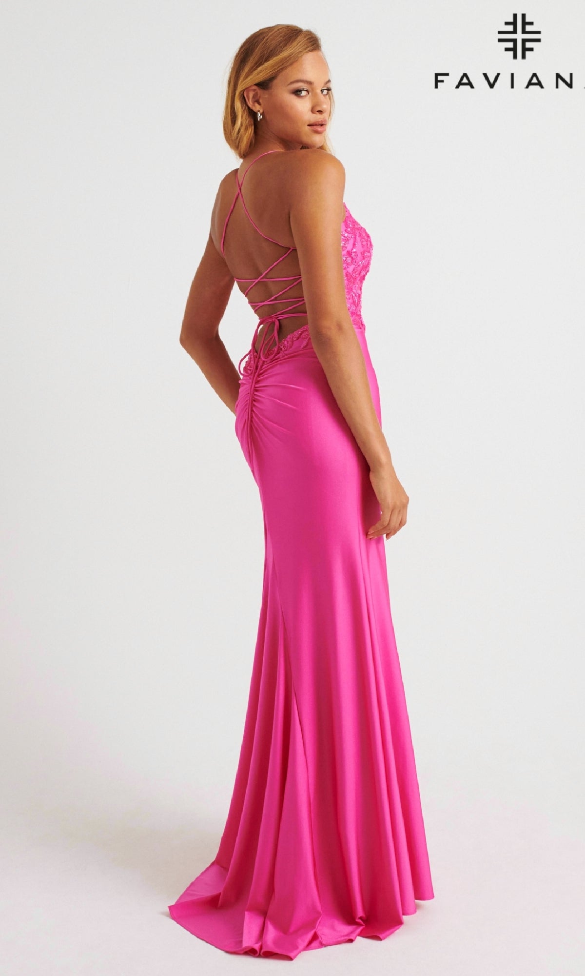 A woman in a vibrant pink, floor-length Faviana 11264 prom dress with a lace-up back stands slightly turned; the sparkling beaded bodice catches the light as the Faviana logo appears in the corner.
